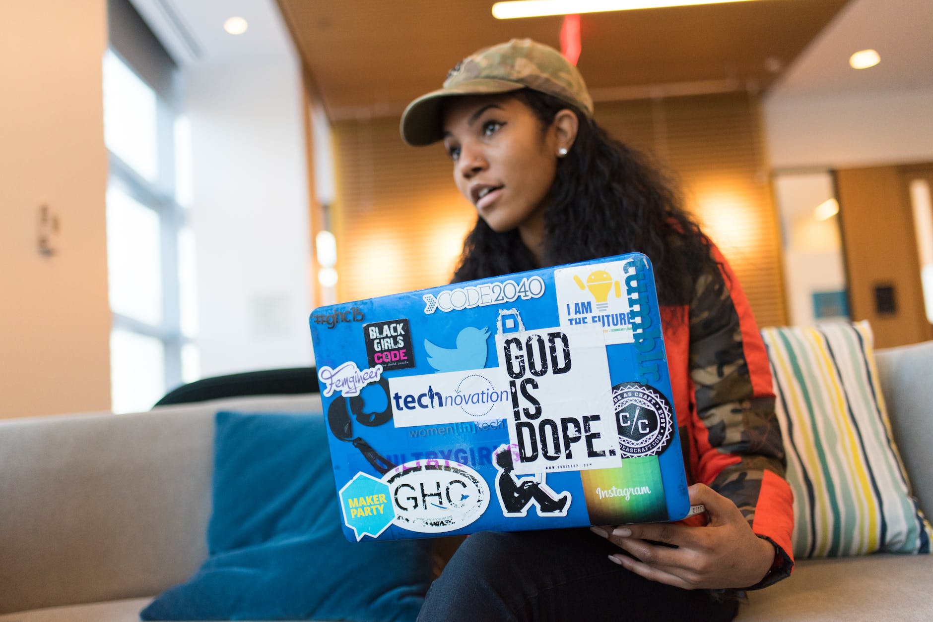 woman holds blue laptop computer while sits on sofa inside the room. stickers over the vent could make your hot laptop