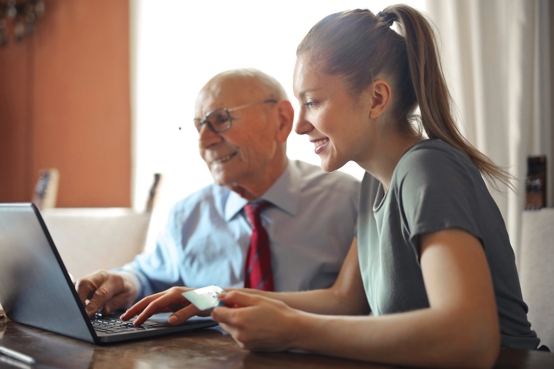 young woman helping senior man with payment on internet using laptop, in our computer shop we make understanding computers fun