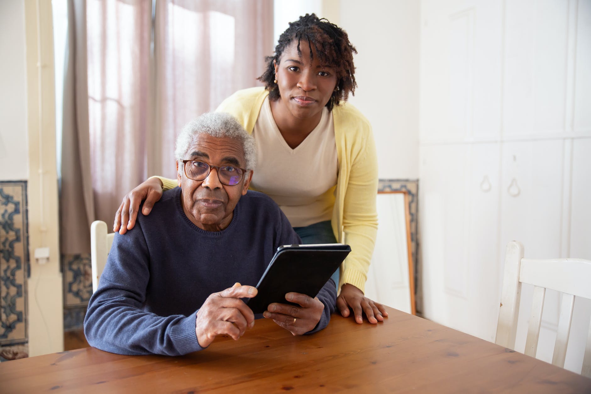 a woman standing beside the elderly man holding a tablet Tech Classes for adults and Seniors